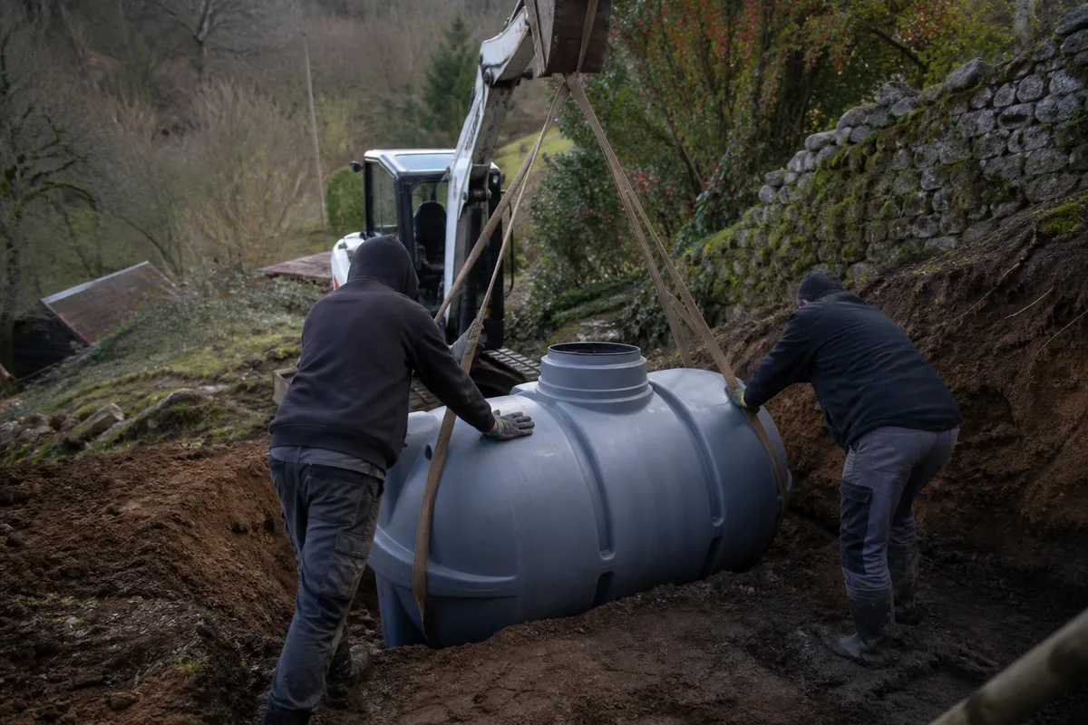 Cuve de fosse toutes eaux en polyéthylène descendue à la mini-pelle dans une fouille sur un terrain en pente