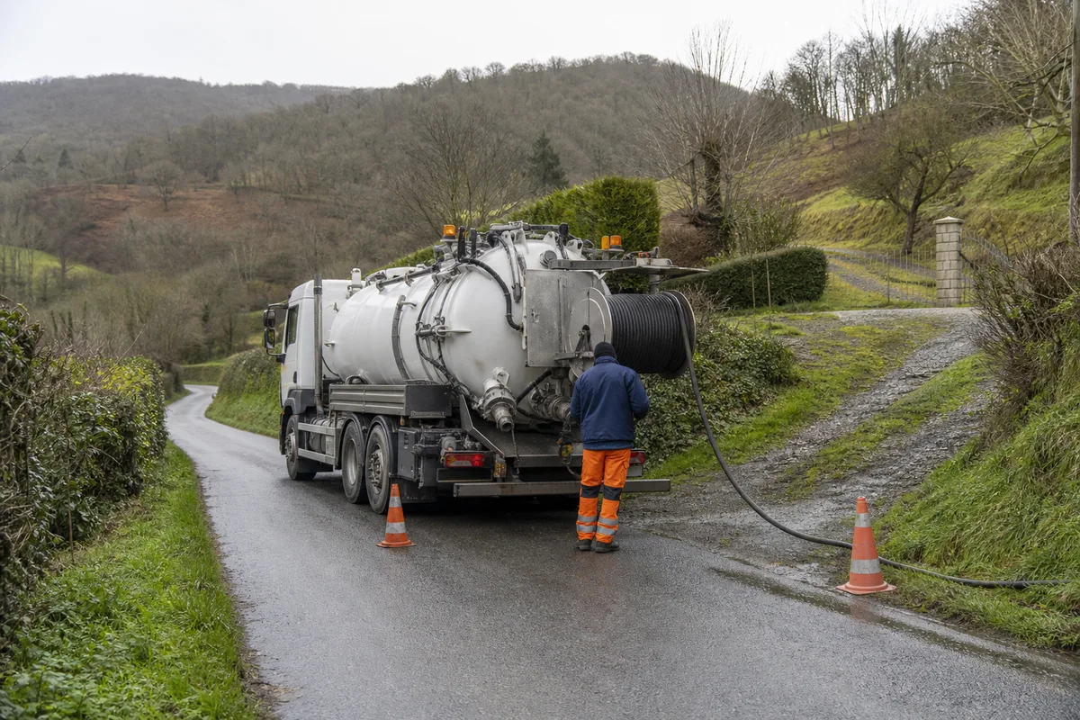 Camion hydrocureur stationné sur une route étroite de vallée verdoyante, flexible déroulé vers un talus